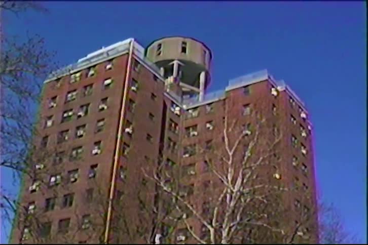 A multistory condo apartment building in the city with a large water tank on top surrounded by leafless trees on a winter day