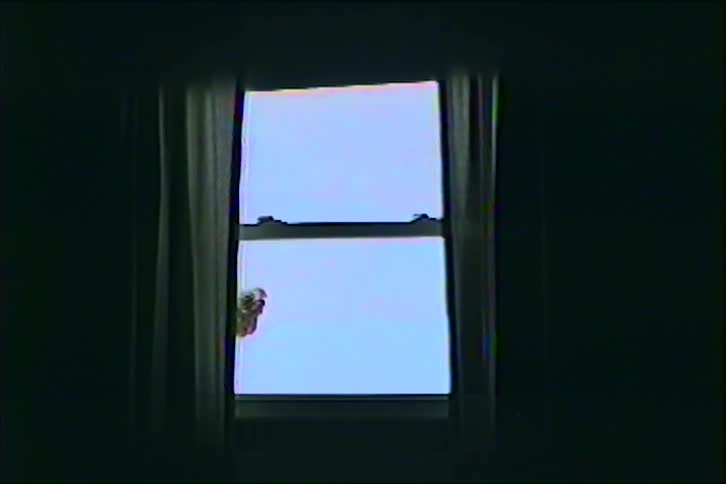 A dim interior frames a bright window with curtains drawn to the sides and the shadow of an object on the window revealing a pale sky outside
