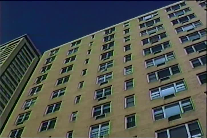 View looking up at a tall apartment building with many windows under a deep blue sky
