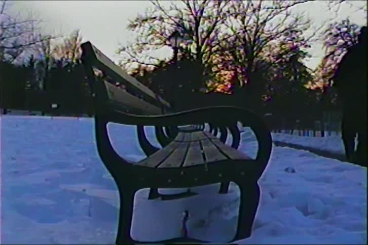 Park bench covered in snow at dusk