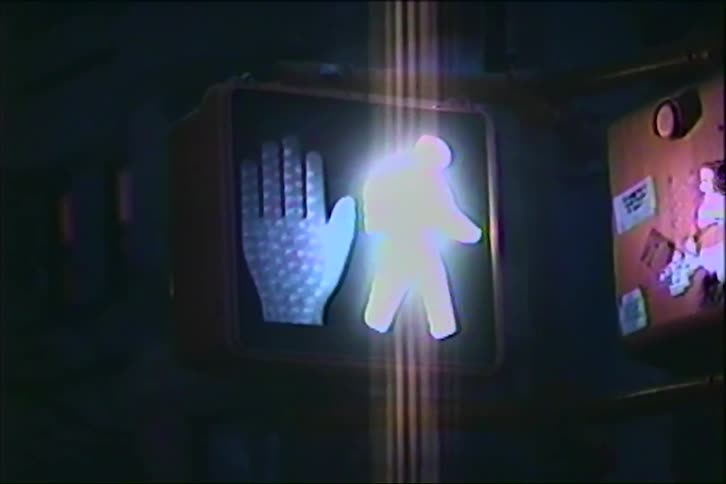A pedestrian crossing signal shows a red hand symbol indicating dont walk against a dark urban background