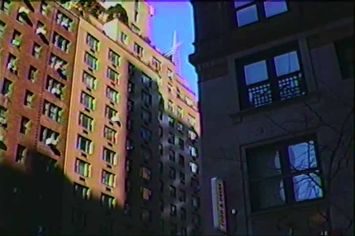 Sunlight hits the side of a tall brick apartment building with many windows in a city setting with a grainy film texture and soft purple and blue light leaks