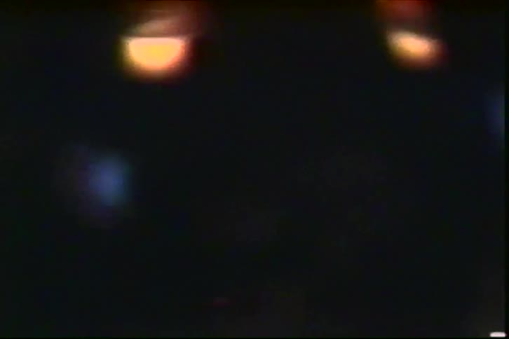 A view of several small round candles flickering with warm orange light in a dark room with a grainy film texture and soft bokeh effects