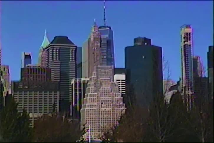 A wide shot of a city skyline with tall buildings seen from across a frozen body of water with trees in the foreground