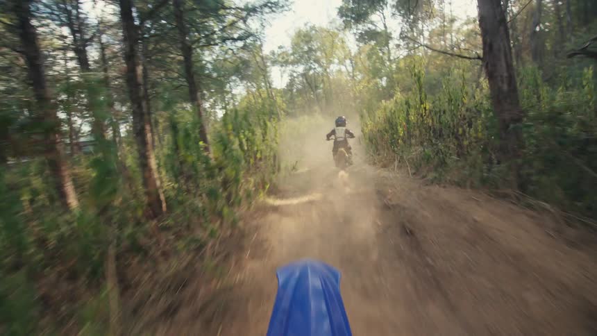 View from a motorbike following another motorbike through trails in the woods