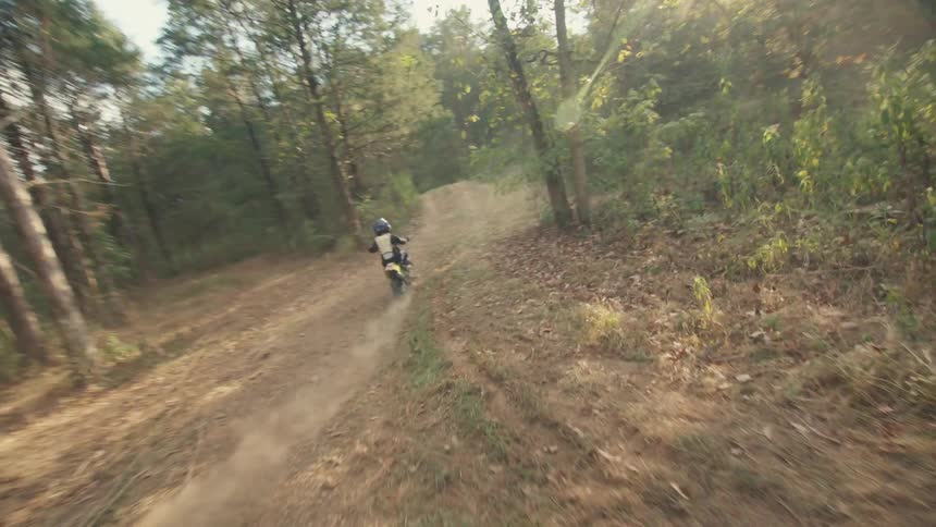 A person wearing a helmet rides a small dirt bike along a winding trail through a wooded area