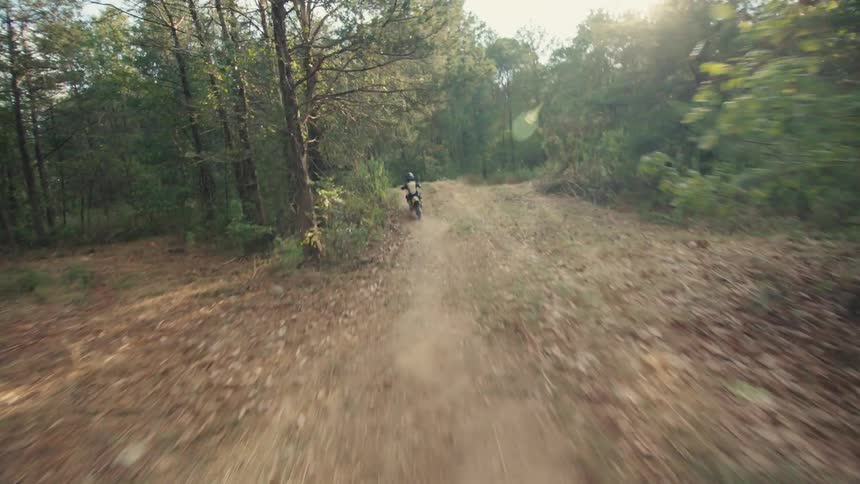 Dirt bike rider rides along a forest dirt trail seen from a distance with dust rising