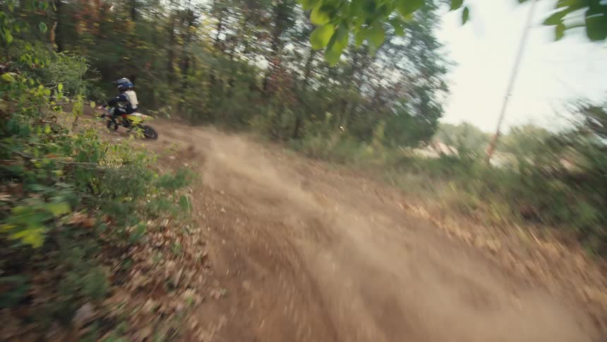 This video features a pointofview perspective of a dirt bike rider chasing another biker down a dusty woodland trail the camera follows closely as both riders navigate sharp turns and kick up plumes of dirt through the sundrenched forest