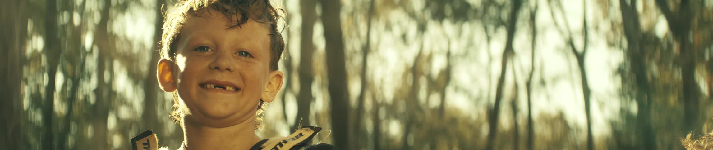 Boy smiling outdoors with blurred trees in the background under golden sunlight