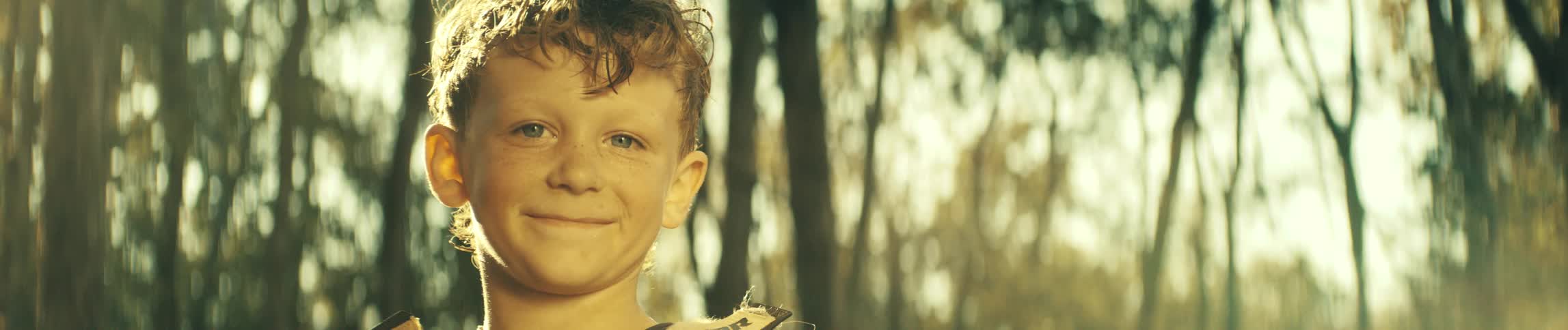 Boy smiles as he stands in the woods