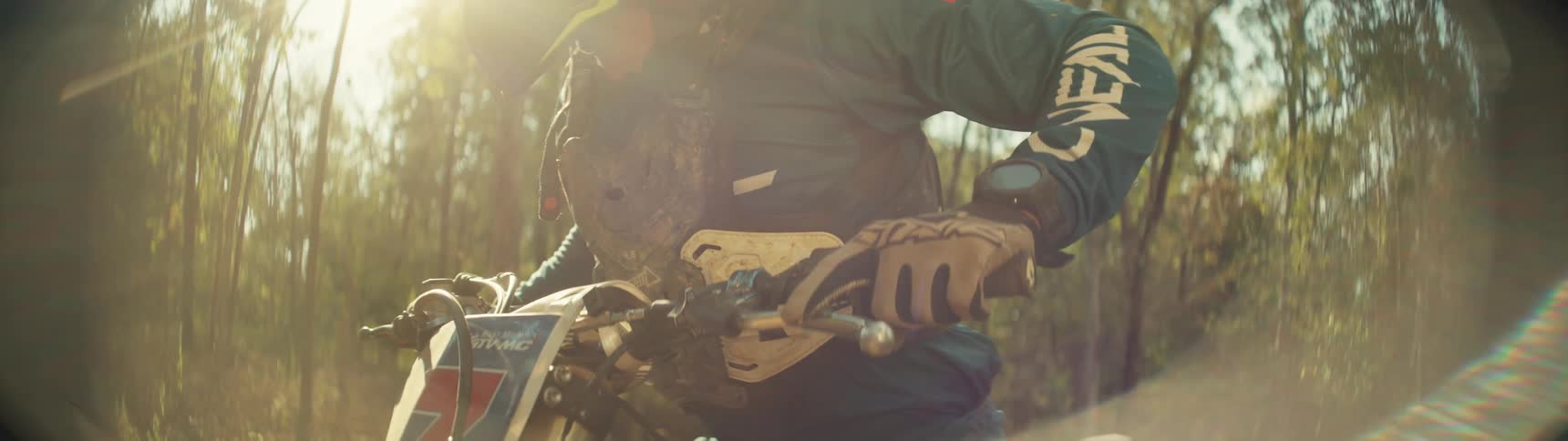 Motorcyclist sits on a dirt bike in the woods on a sunny day