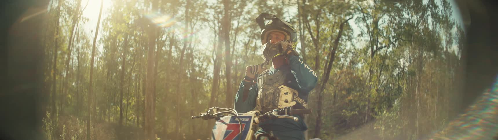 A male biker wearing his helmet while sitting on his bike in the woods at midday