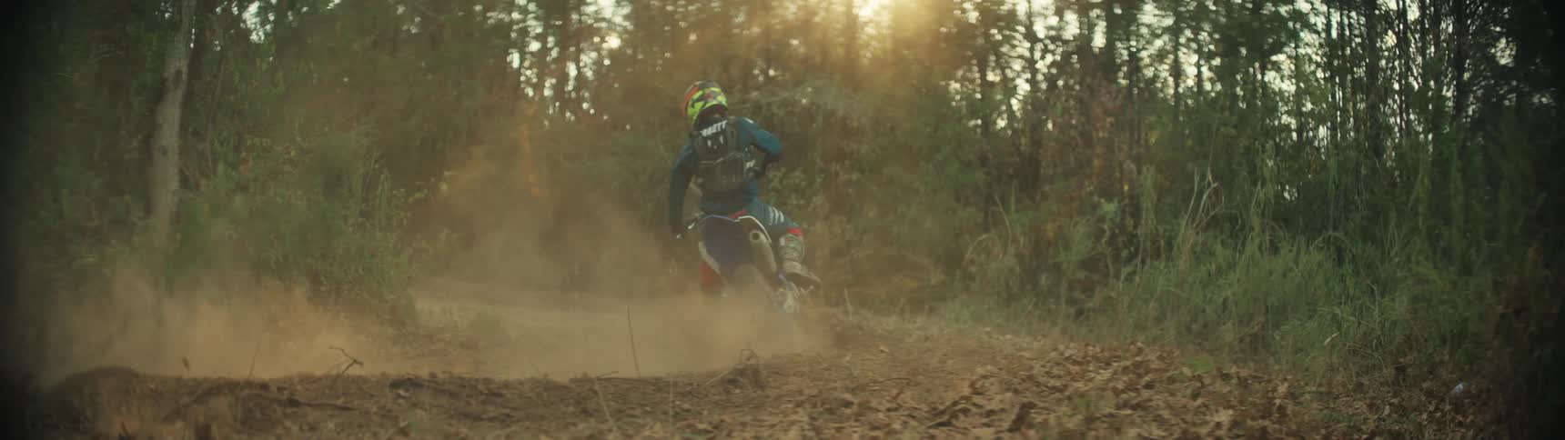 Dirt bike rider takes a turn on a forest dirt trail kicking up dust under sunlight