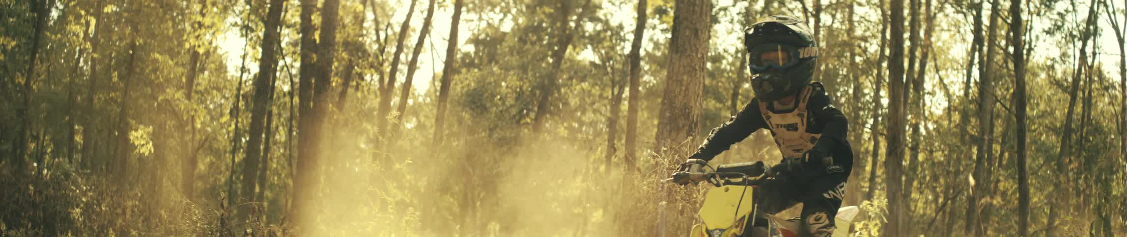 A person wearing yellow ppe and a helmet rides a bike in the woods during a mountain biking competition at midday