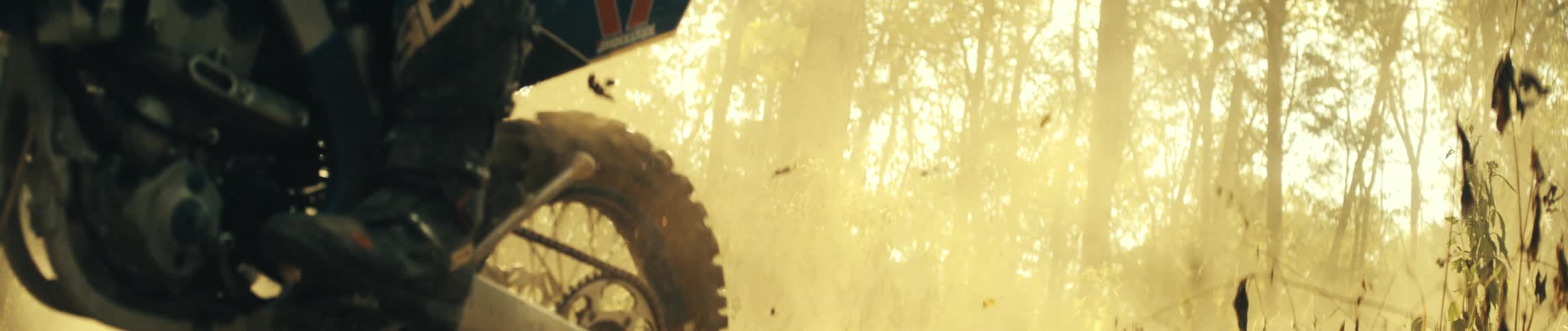 Motorcyclist rides through the woods filling the air with fallen leaves and dust during the daytime