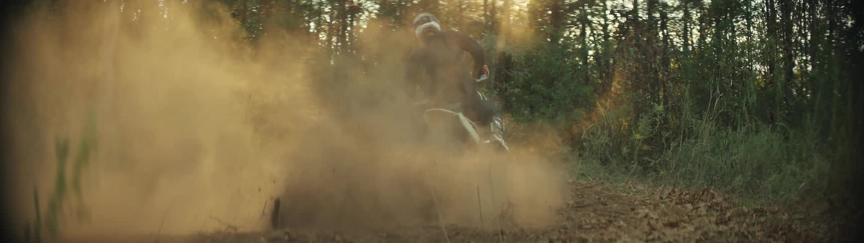Motocross bikers wearing helmets riding motorcycles in a forest and raising dust outdoors during day time