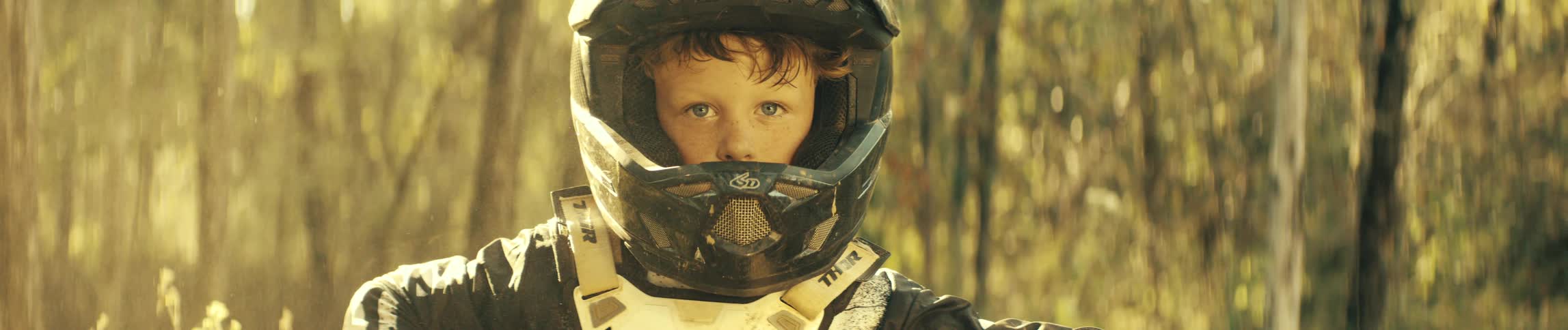 The boy is wearing motocross protective gear in the forest