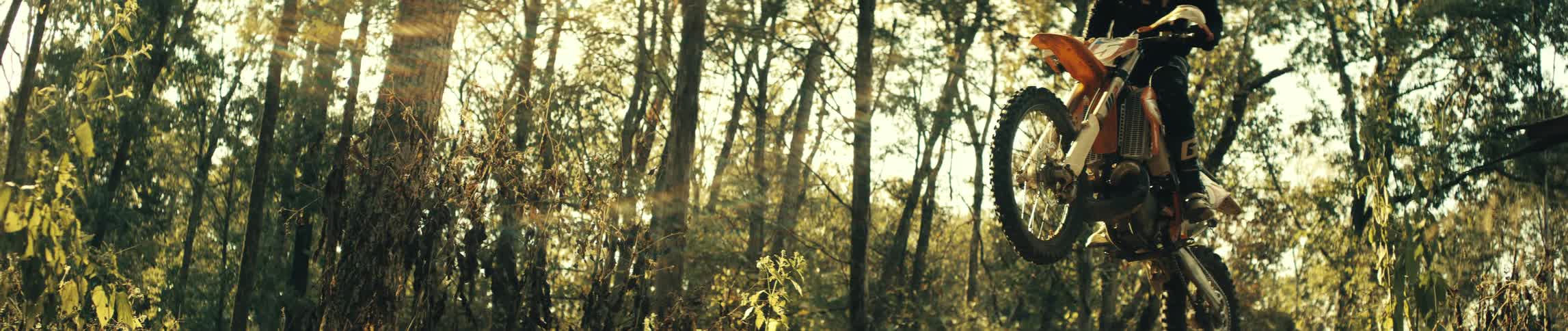 Dirt bike rider jumps on a forest trail under sunlight among trees
