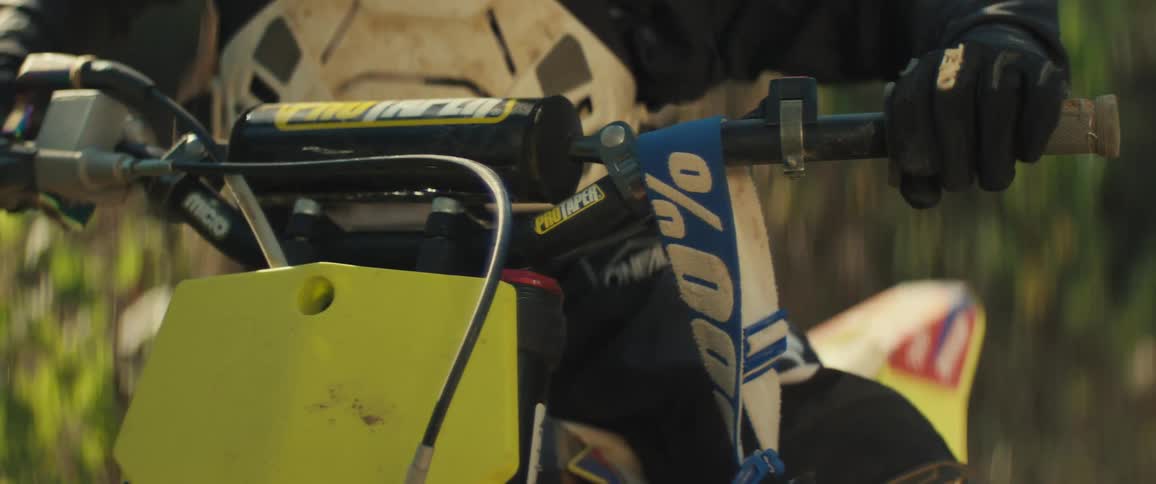 A person seated atop a dirt bike reaches for their goggles