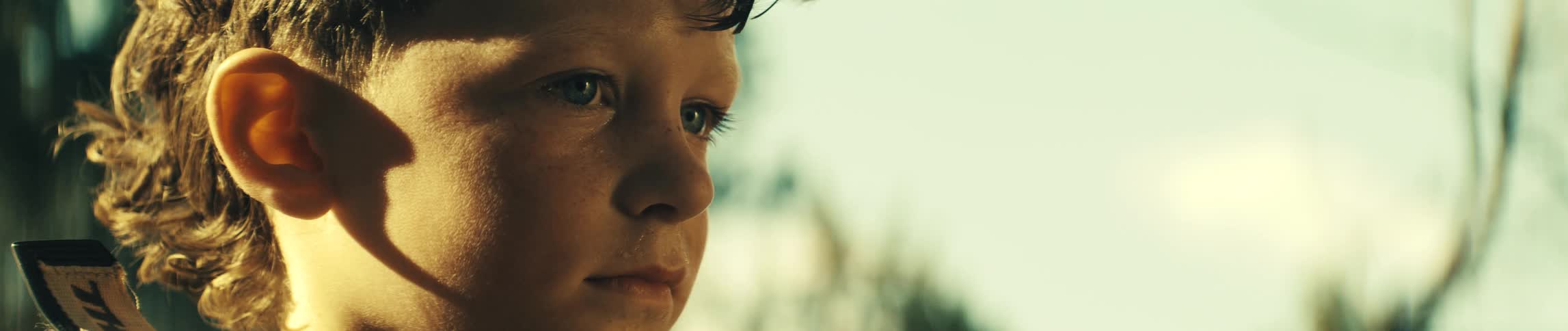 A close view of a young boy with light eyes looking off to the side with a calm expression against a bright background