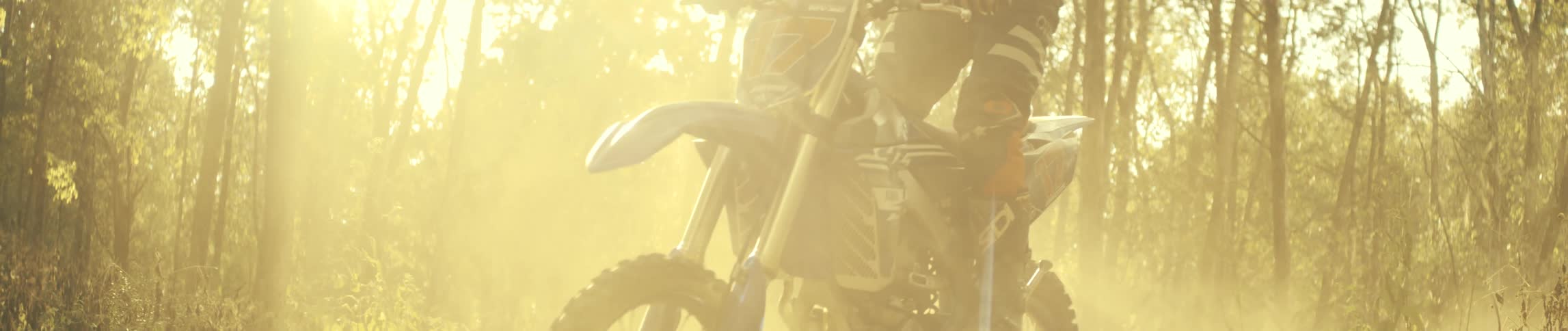 The dirt bike gives off a dust cloud in the forest