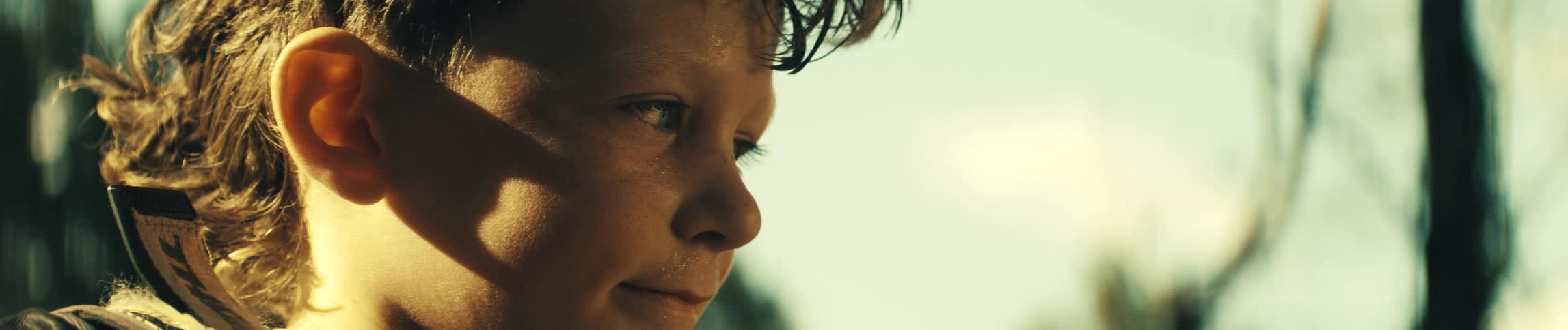 A close view of a young boy with light eyes and wet hair looking off to the side with a calm expression against a bright background