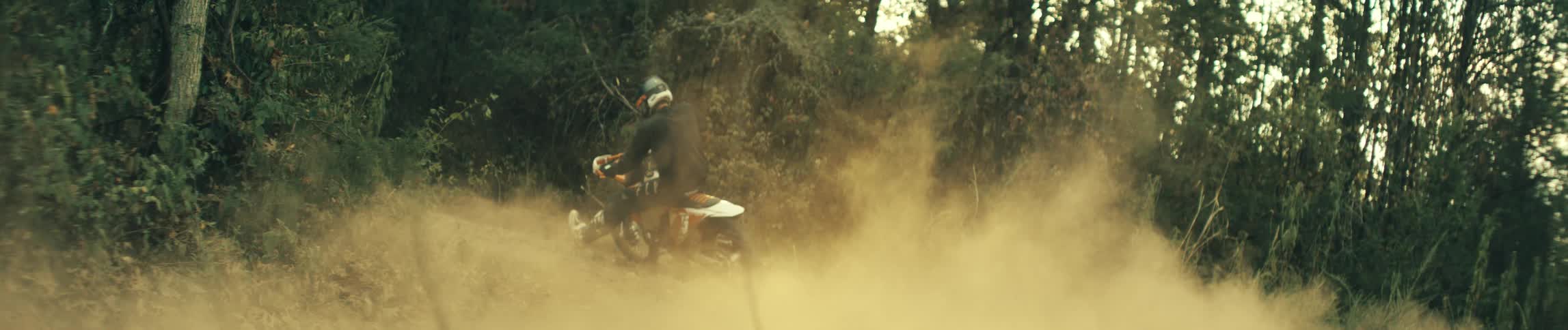 Motorcyclist rides a motorcycle through the woods on an autumn day creating a cloud of dust