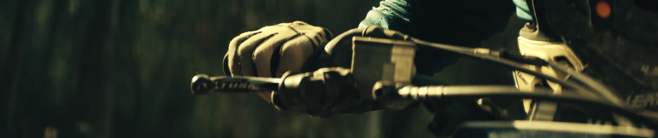 Gloved hand grips the handlebars of a dirt bike in an outdoor setting with trees in the background