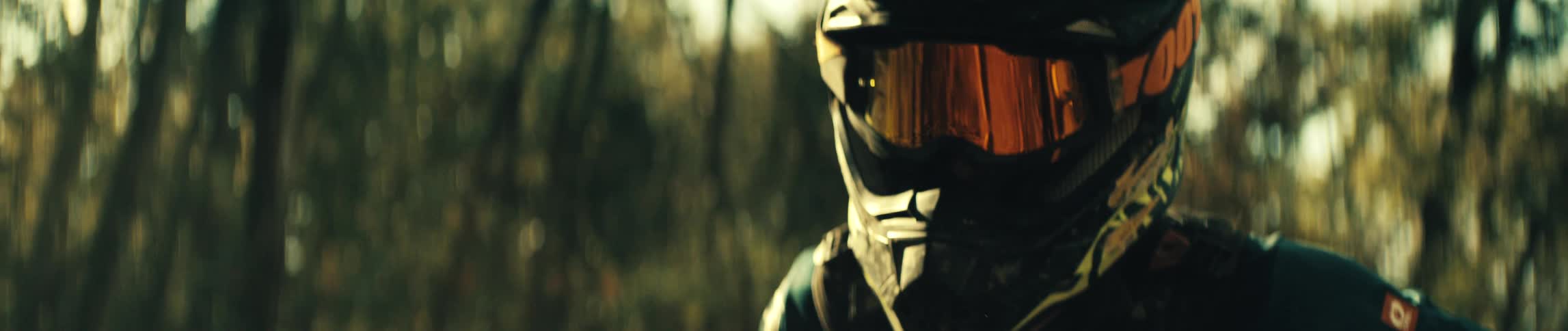 Person wears a motocross helmet with mirrored visor in an outdoor setting with trees in the background