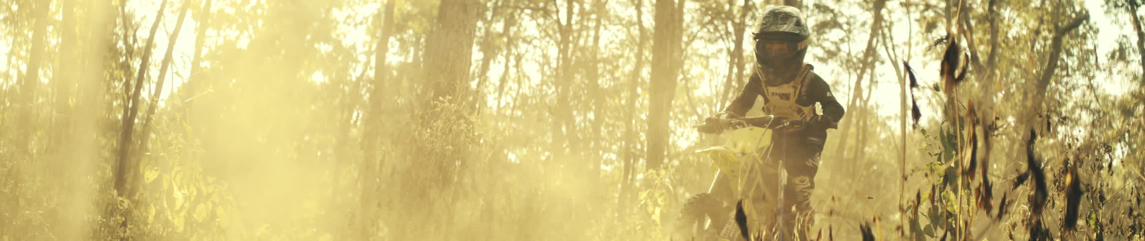 A person drives a dirt bike along a forest trail on a sunny day