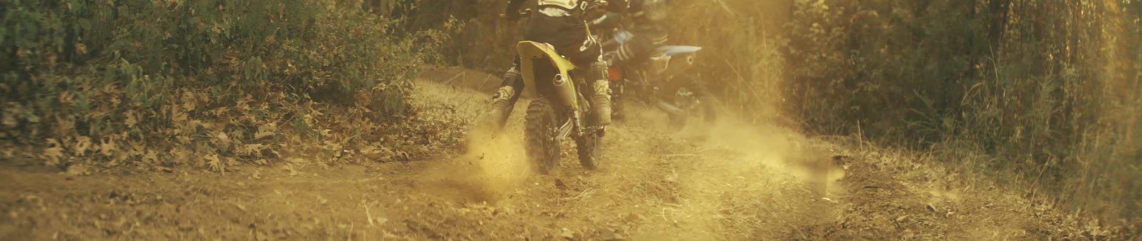 Two mountain bikers riding in the woods as dust fills the air behind them during a competitive race