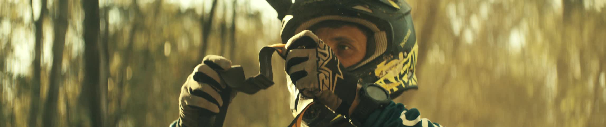Person removes the visor of a motocross helmet in an outdoor setting with trees in the background