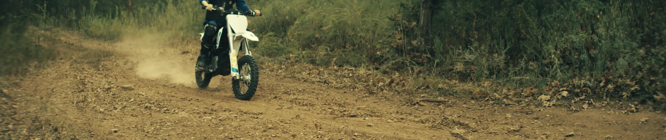 Motorcyclist kicks up dust while riding on a dirt path through the woods