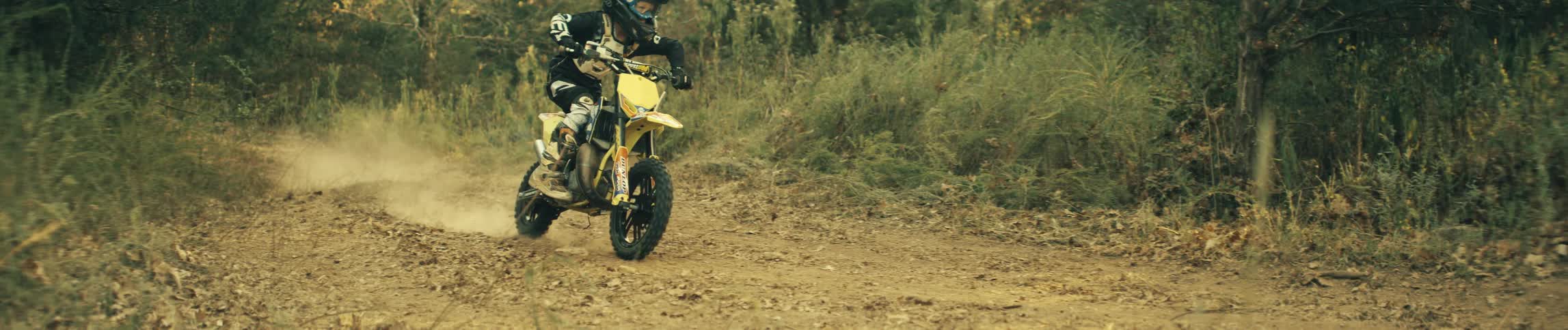 A mountain biker riding through rough terrain in the woods on his yellow bike wearing a helmet at midday