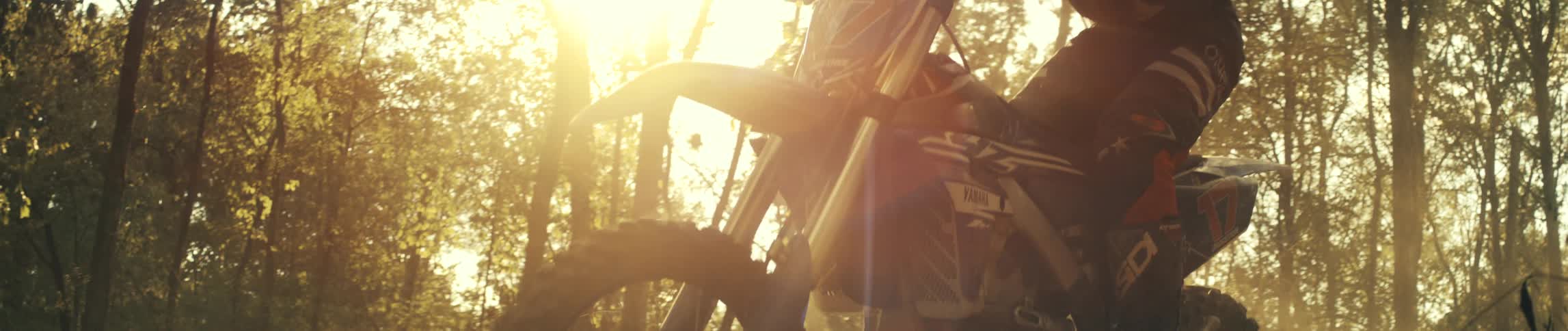 Person rides a dirt bike under strong sunlight on a forest trail