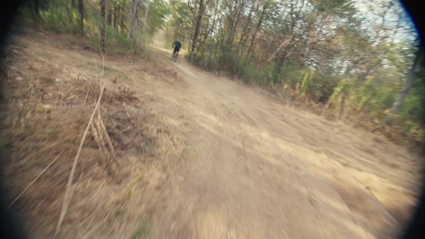 This firstperson pointofview shot captures the intense speed of a dirt bike racing through a dusty wooded trail the rider navigates sharp turns and small jumps while closely pursuing another biker ahead