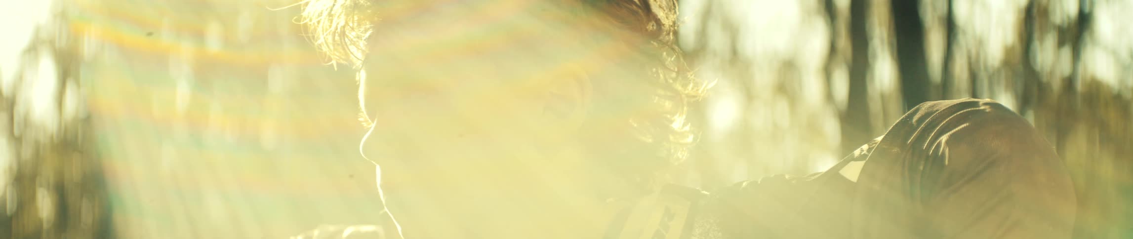Boy with a serious expression outdoors under golden sunlight with blurred trees in the background