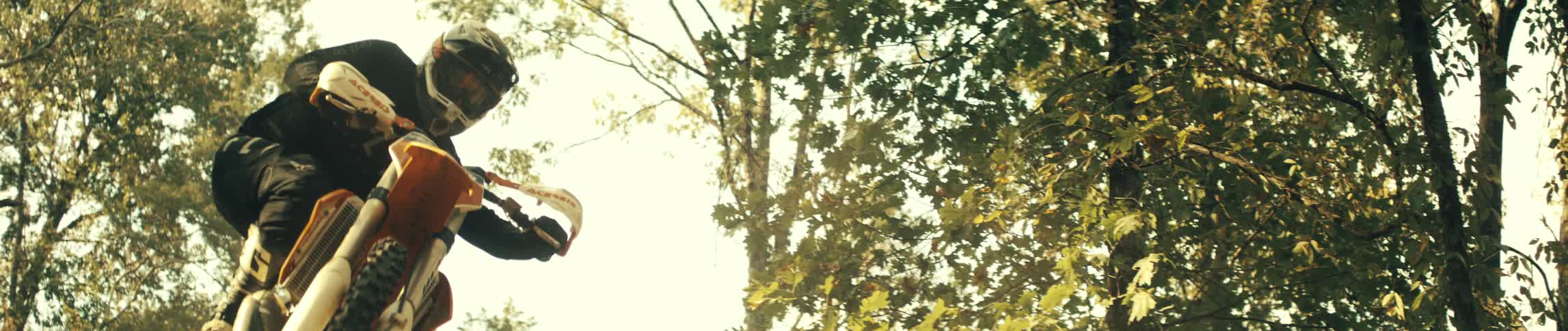 Dirt bike rider jumps on a forest trail under strong sunlight among trees