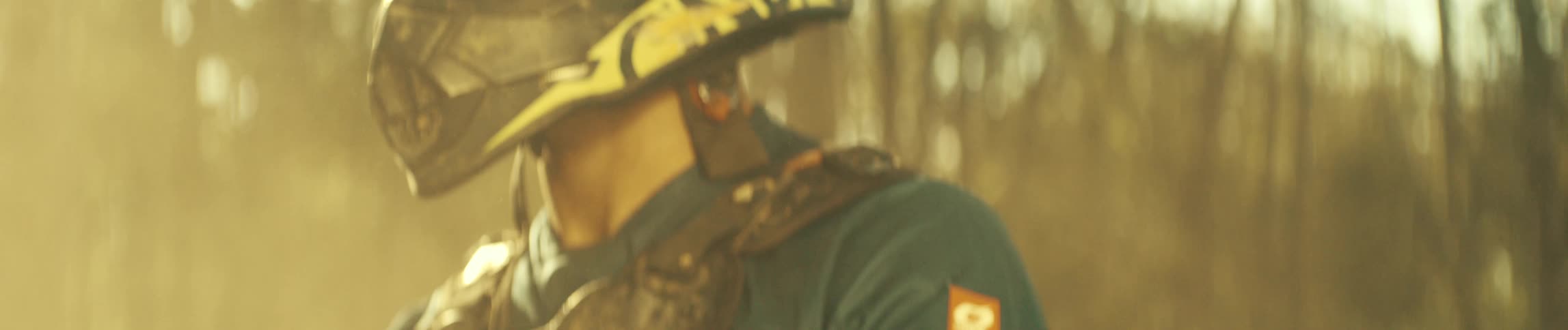 A close up shot of a male motocross rider in a dirty helmet and gear panning down to his gloved hand on a handlebar with a smartwatch