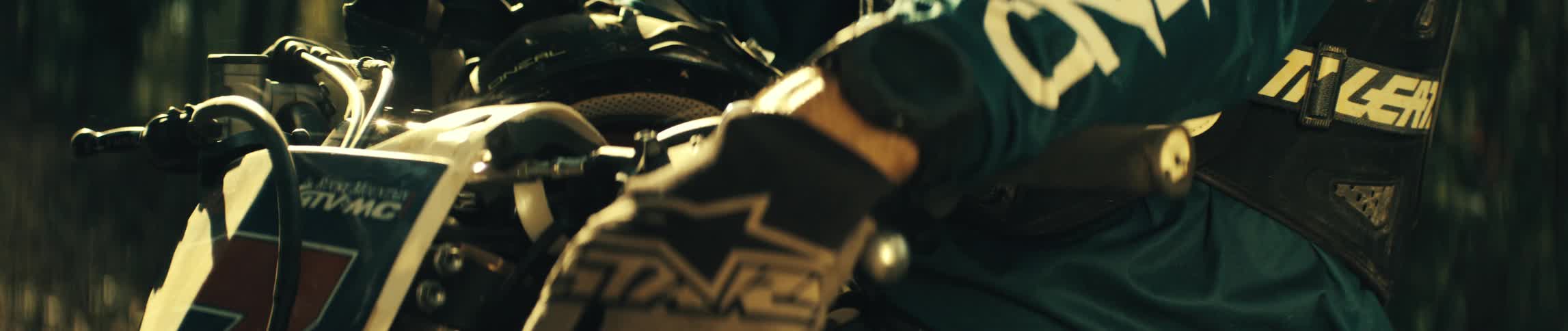 Gloved hand rests on the handlebars of a dirt bike under sunlight outdoors