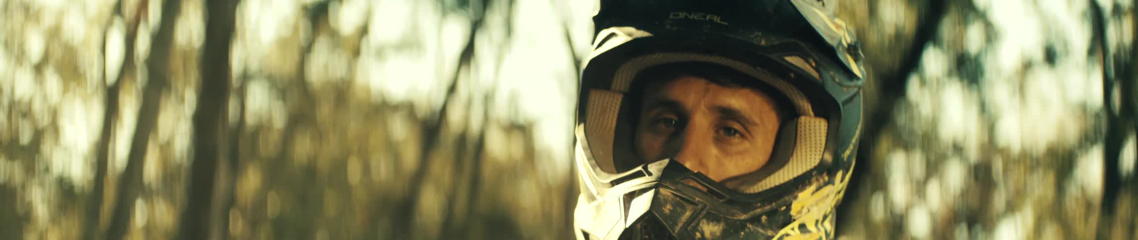 A man wearing a black and yellow helmet removes his goggles while looking directly ahead with a serious expression in a close view during a sunny day