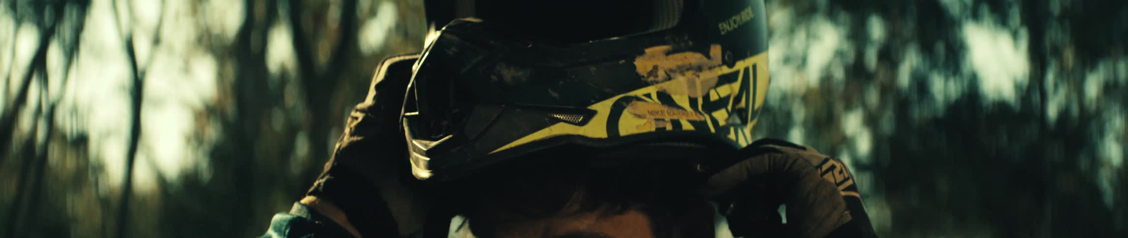 Wearing thick racing gloves a man slowly pulls a scratched dirtspeckled motocross helmet down over his head his focused expression emerging into the warm light