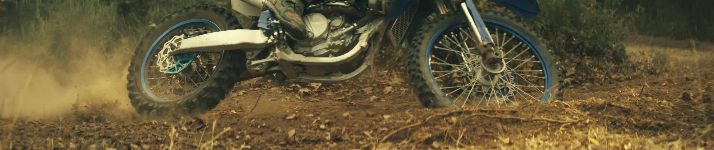 Motorcyclist rides along a dirt path through the woods during the daytime