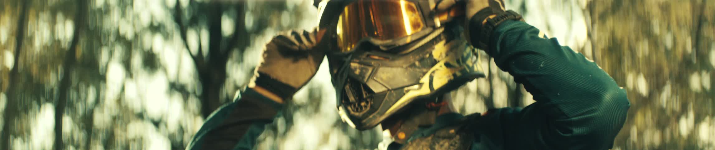 Motorcyclist adjusting a helmet with a reflective visor outdoors under golden sunlight