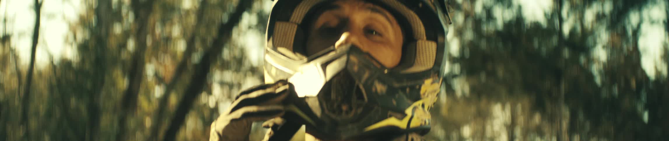 A man wearing gloves puts on a yellow and black patterned helmet while looking down in a close view with soft natural light in the background