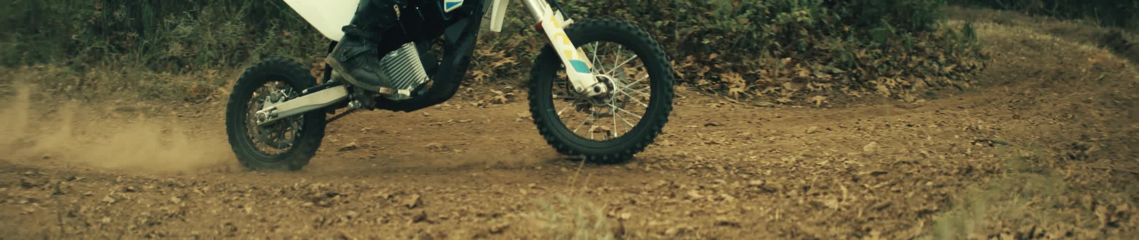 Dirt bike wheel moves along a forest dirt trail kicking up dust