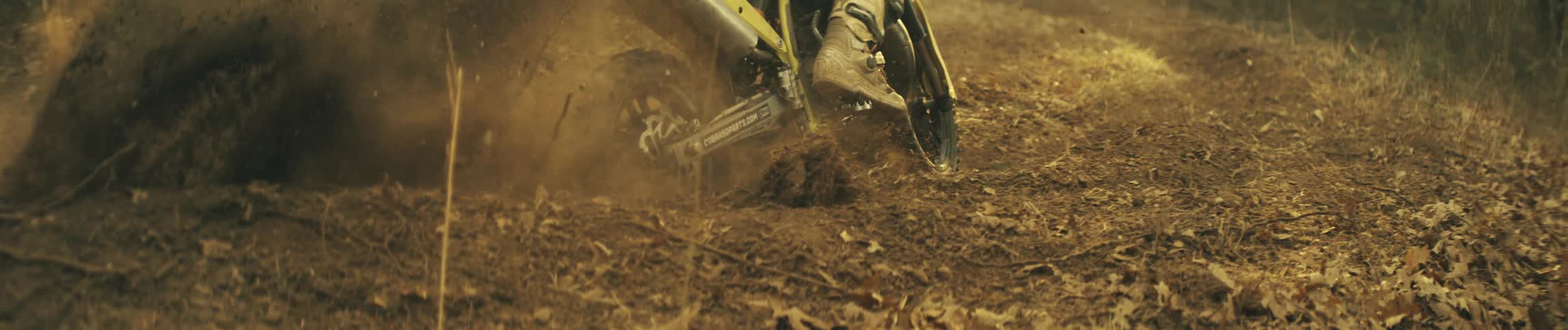 Dirt bike wheel moves along a forest dirt trail kicking up dust and dry leaves