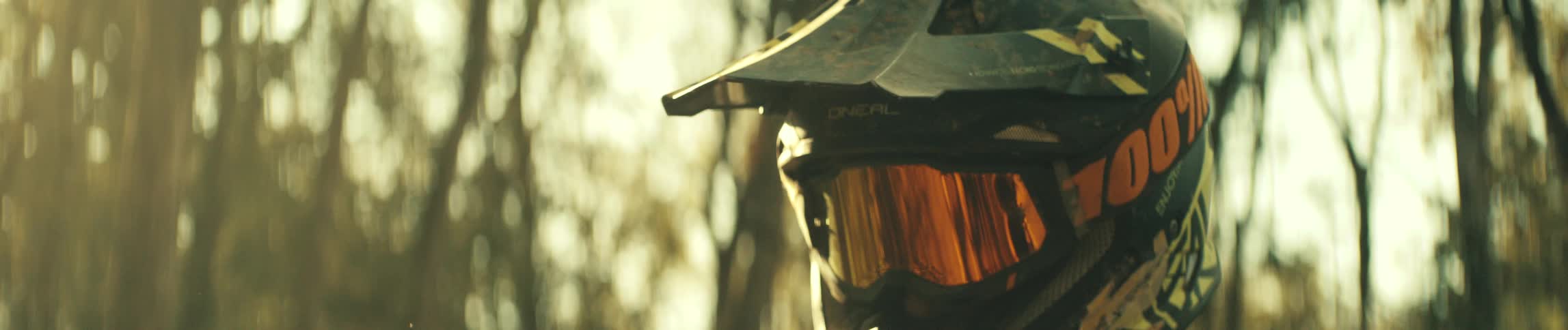 A mountain biker in the woods wearing a helmet and goggles surrounded by trees at midday
