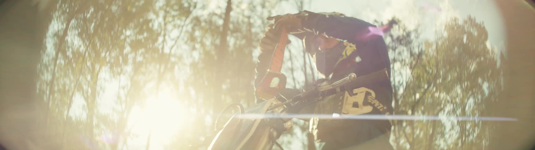 Motorcyclist puts on his helmet while sitting on his motorcycle under the bright sunlight in the forest