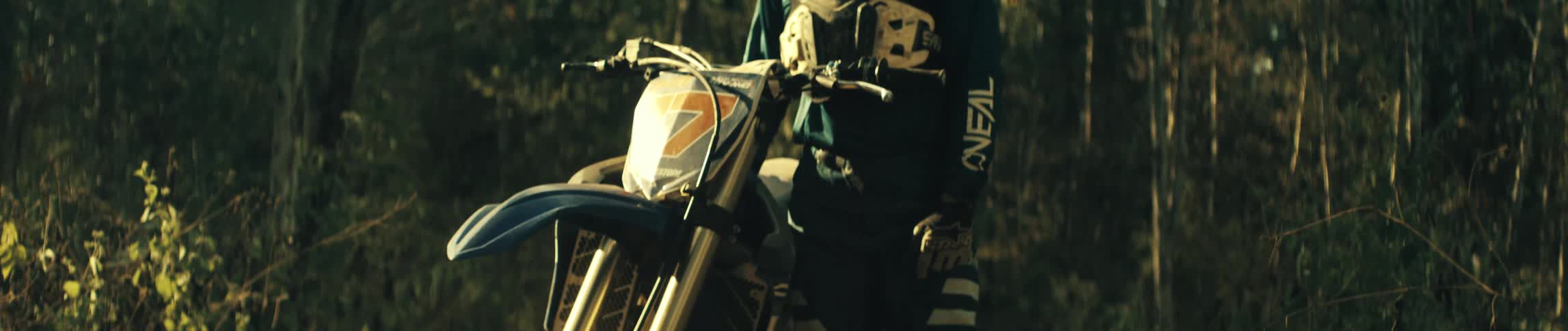 Motorcyclist stands next to his motorcycle in the woods on an autumn day